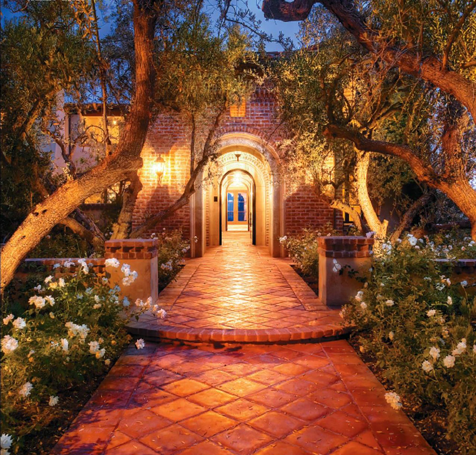 tile and brick front entryway with flower beds and landscaped trees